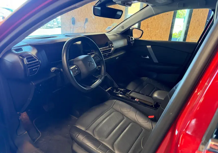 Vue intérieure côté conducteur de la Citroën C4 X rouge, avec sièges en cuir noir et tableau de bord moderne.