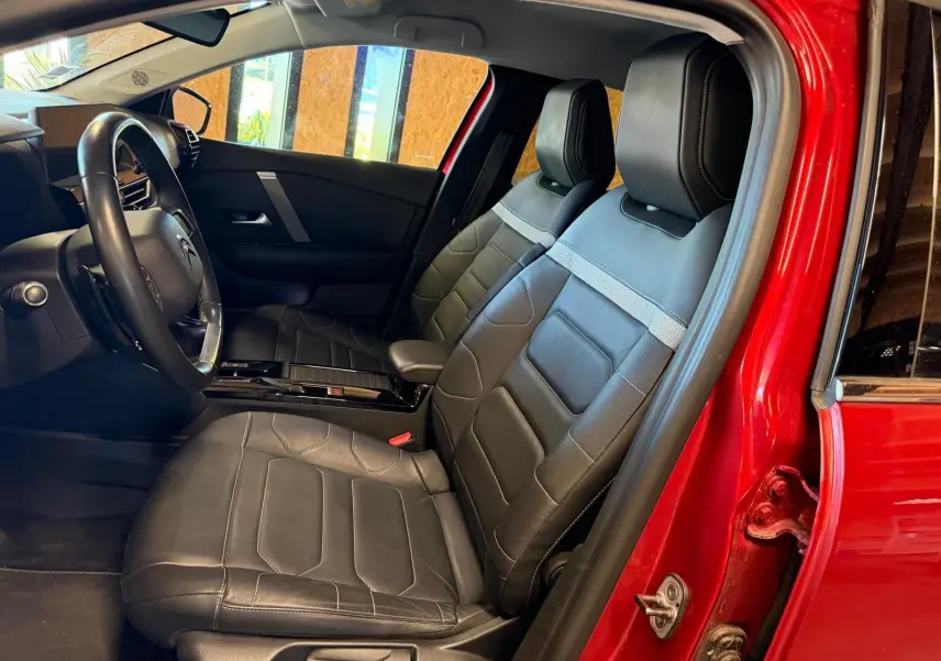 Vue intérieure côté conducteur de la Citroën C4 X rouge 2021, sièges avant en cuir noir avec surpiqûres grises.