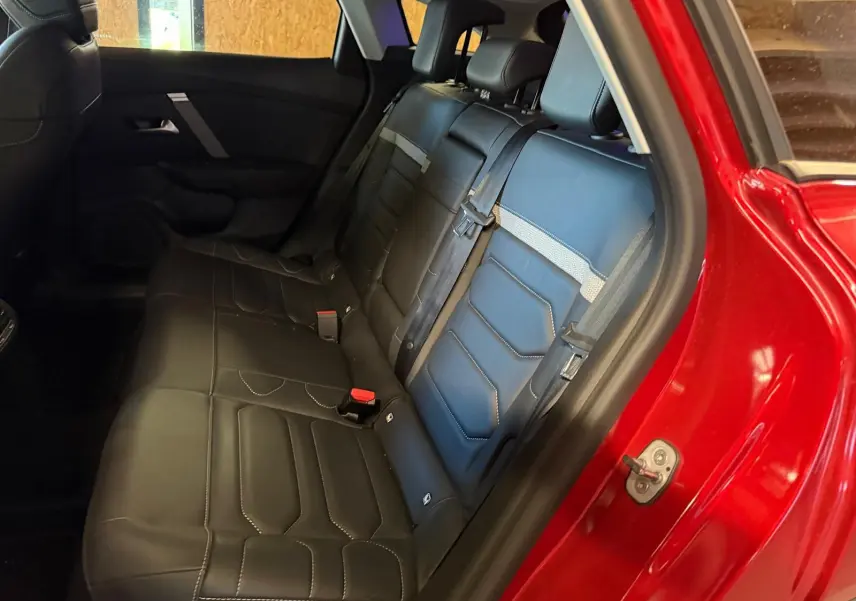 Vue intérieure côté gauche des sièges arrière en cuir noir de la Citroën C4 X rouge, avec ceinture de sécurité attachée.