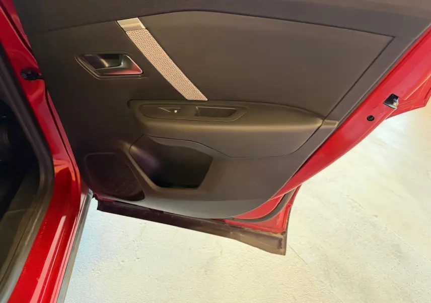 Vue rapprochée de la porte arrière gauche rouge du Citroën C4 X avec garniture intérieure noire et bande décorative claire.