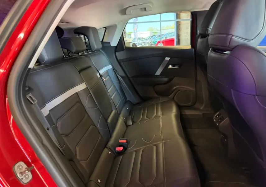 Vue intérieure côté arrière gauche montrant les sièges arrière en cuir noir avec surpiqûres blanches d'une Citroën C4 X rouge.