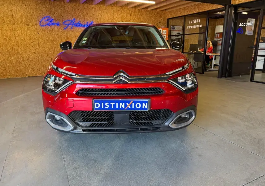 Vue de face d'une Citroën C4 X rouge 2021, avec calandre chromée et plaque Distinxion, en intérieur showroom.