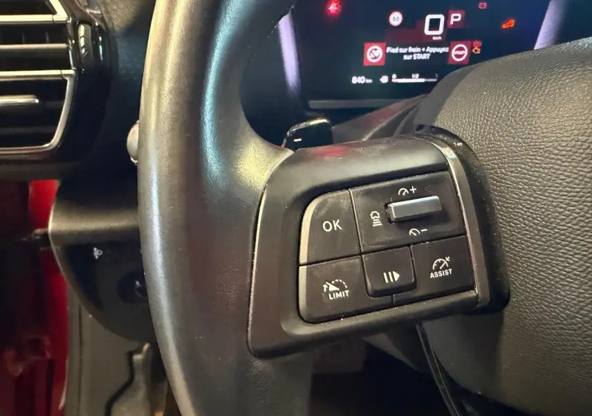 Gros plan sur les commandes au volant côté gauche d’une Citroën C4 X 1.5 BlueHDi 130 diesel, tableau de bord numérique en arrière-plan.