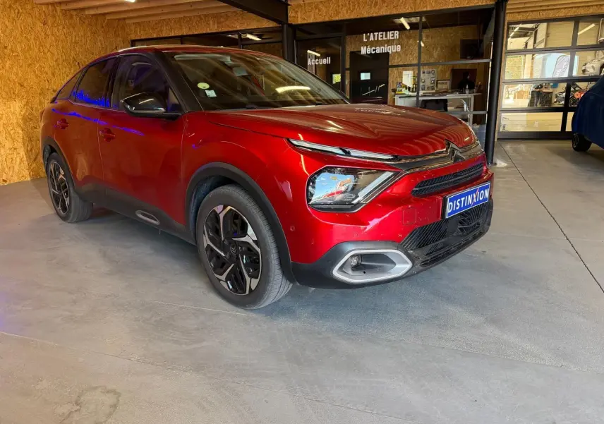 Vue 3/4 avant droite d'une Citroën C4 X rouge métallisé stationnée dans un garage avec détails noirs contrastants.