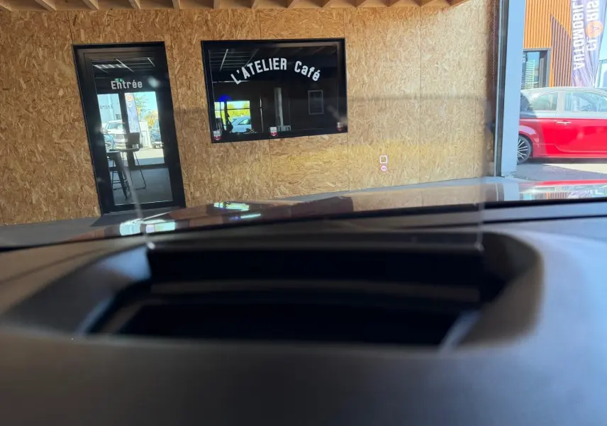 Vue depuis l'intérieur du Citroën C4 X 2021, montrant le tableau de bord et le pare-brise face à un mur en bois clair.