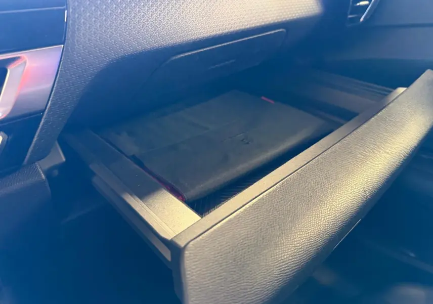 Gros plan sur la boîte à gants ouverte de la Citroën C4 X 1.5 BlueHDi 130, intérieur noir en tissu.