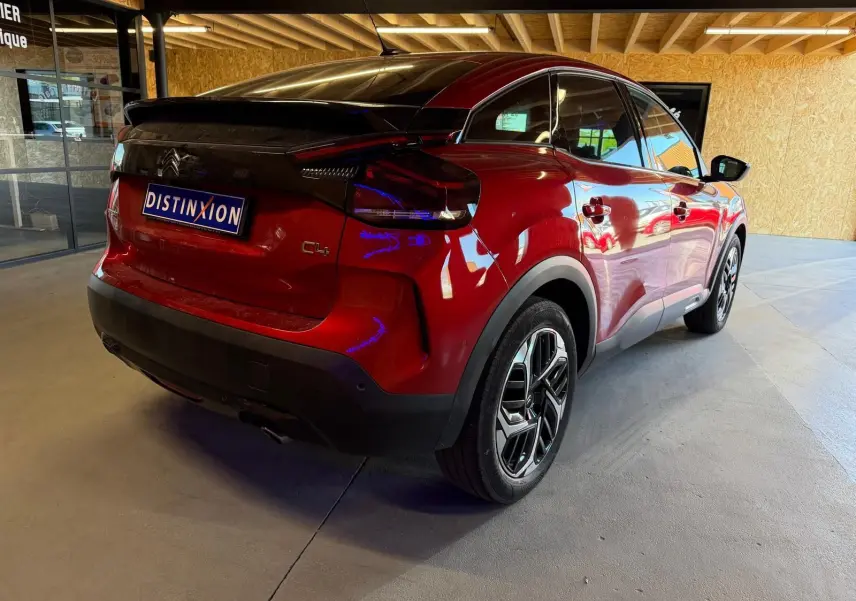 Vue 3/4 arrière droite d'une Citroën C4 X rouge métallisé avec toit noir et jantes alliage distinctives.