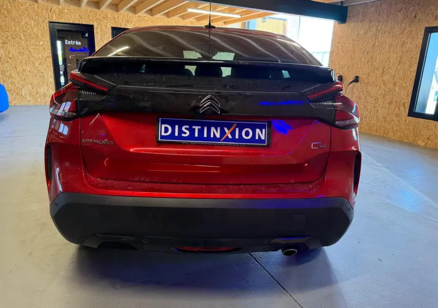 Vue arrière d'une Citroën C4 X rouge avec toit noir, dans un garage aux murs en bois clair.