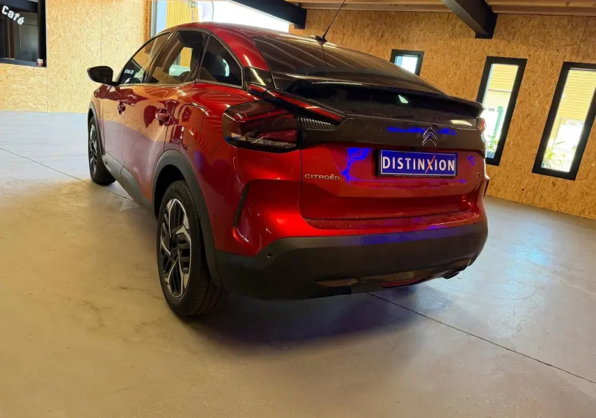 Vue 3/4 arrière droite d'une Citroën C4 X rouge métallisé avec toit noir dans un garage lumineux.