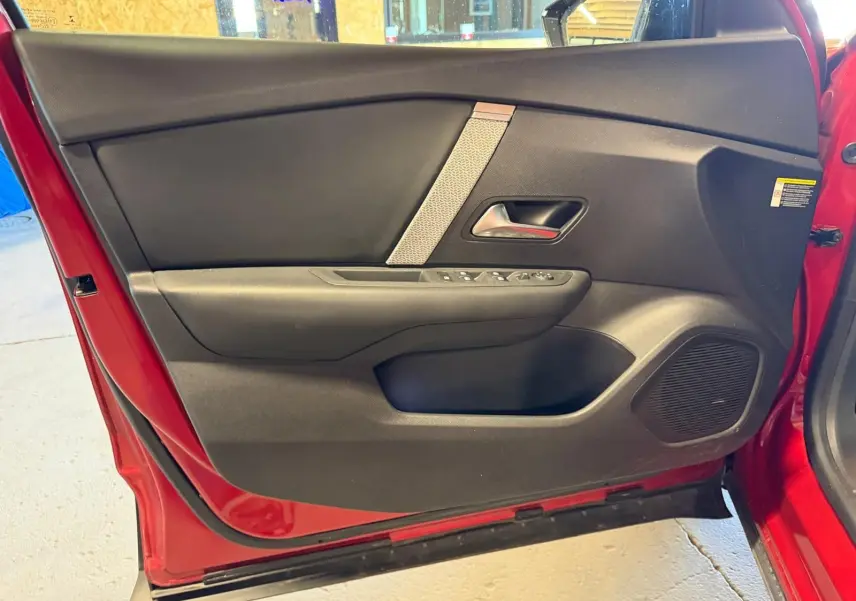 Vue intérieure de la porte avant gauche rouge d'une Citroën C4 X 2021 avec garniture noire et commandes de vitres.