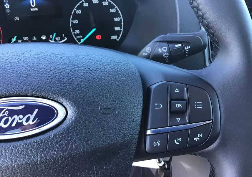 Gros plan sur le volant noir du Ford Transit Châssis Cabine 2024 avec commandes multifonctions et tableau de bord digital.