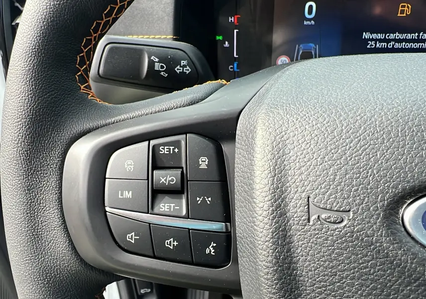 Gros plan sur le volant cuir noir du Ford Ranger blanc glacier, avec commandes multifonctions et tableau de bord numérique.