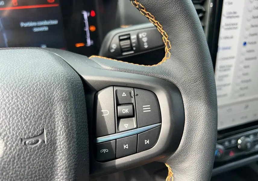 Gros plan sur les commandes multifonctions du volant en cuir noir avec surpiqûres orange du Ford Ranger blanc glacier 2025.