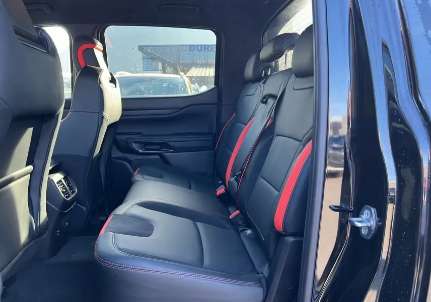 Vue latérale intérieure arrière droite du Ford Ranger Raptor noir absolu, sièges cuir noirs avec surpiqûres rouges.
