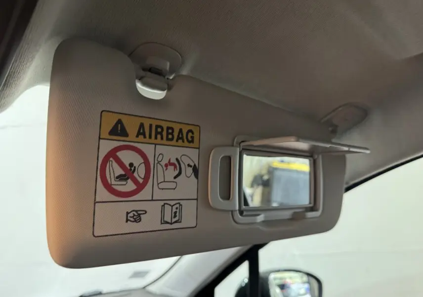 Détail intérieur du pare-soleil côté conducteur avec miroir de courtoisie et avertissement airbag dans une Renault Clio noire.