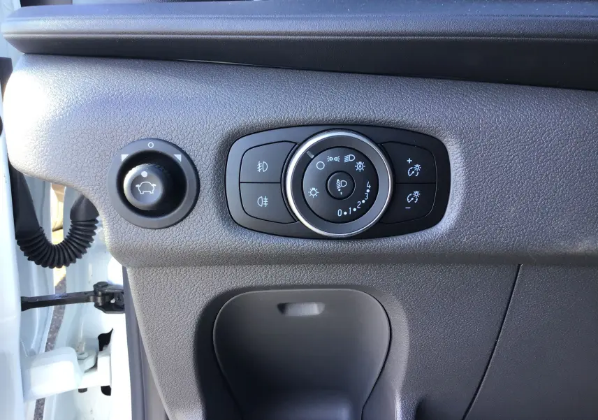 Vue rapprochée des commandes d'éclairage et réglage du tableau de bord sur le côté gauche d'un Ford Transit blanc.