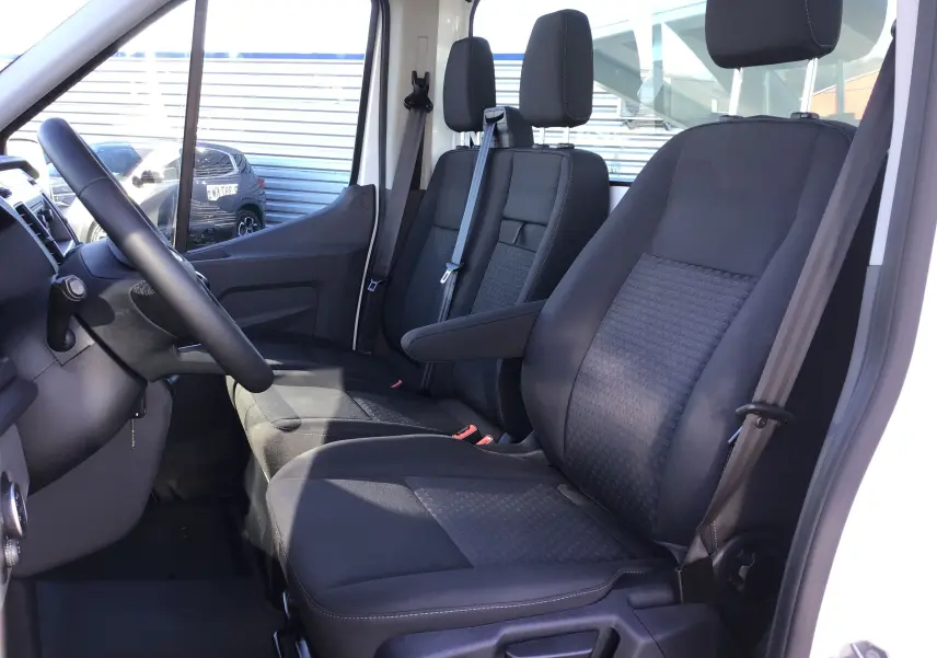 Vue intérieure côté conducteur du Ford Transit Châssis Cabine blanc 2024, montrant les sièges noirs et le volant multifonction.