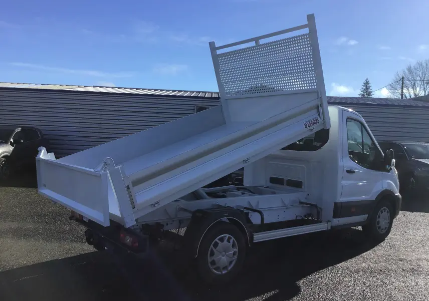 Vue 3/4 arrière droite du Ford Transit Châssis cabine blanc avec benne basculante levée sous un ciel bleu.