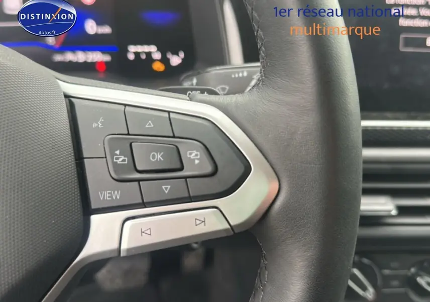 Gros plan sur les commandes multifonctions à gauche du volant cuir d’une Volkswagen Polo gris cendre, tableau de bord numérique visible.