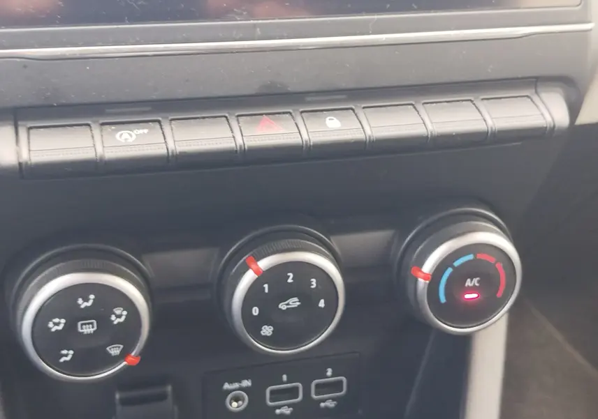 Gros plan sur les commandes de climatisation et boutons de fonction du tableau de bord d’une Renault Clio bleu Iron.