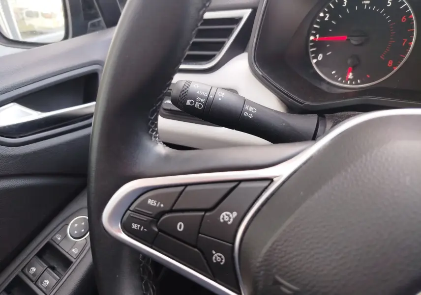 Vue rapprochée du volant côté gauche d’une Renault Clio 2022 bleu Iron, avec commandes au volant et commodo d’éclairage visibles.