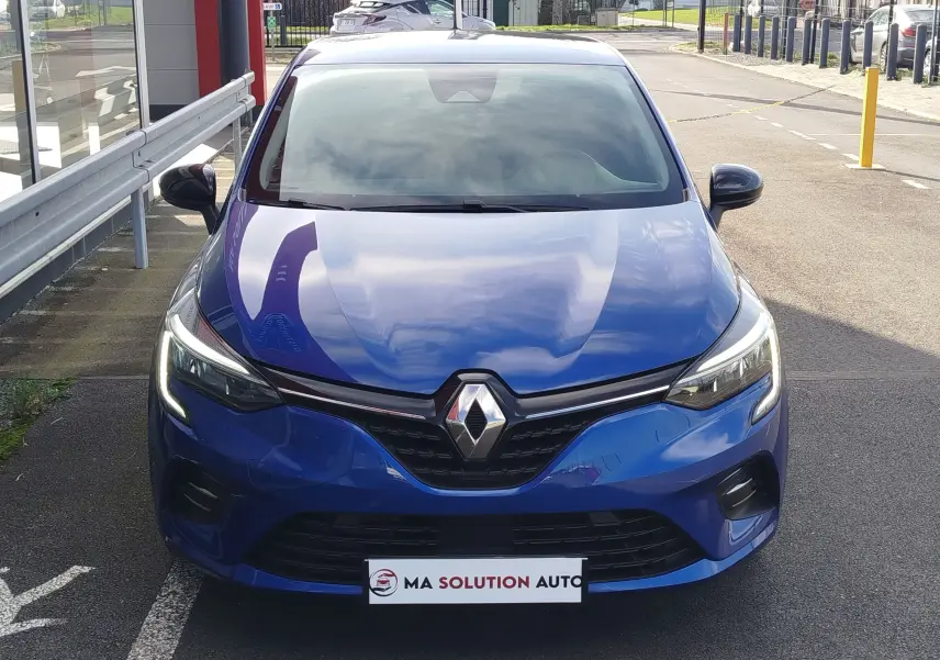 Vue de face d'une Renault Clio 1.0 SCe 65ch Evolution bleu Iron avec phares LED allumés, stationnée en extérieur.