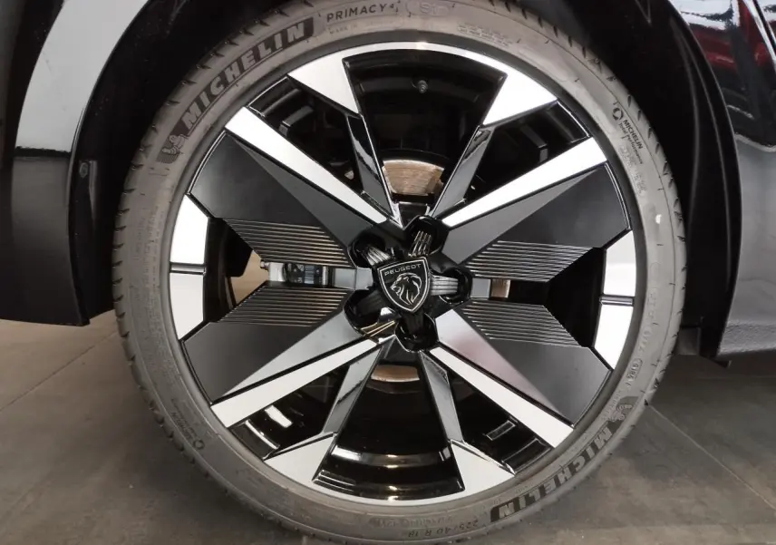 Gros plan sur la jante alliage 18" bi-tons noir et argent avec logo Peugeot, sur roue avant d'une 308 noire.