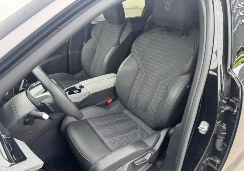 Vue intérieure côté conducteur du Peugeot 5008 Hybrid noir 2025, sièges en tissu et cuir avec logo Peugeot brodé.