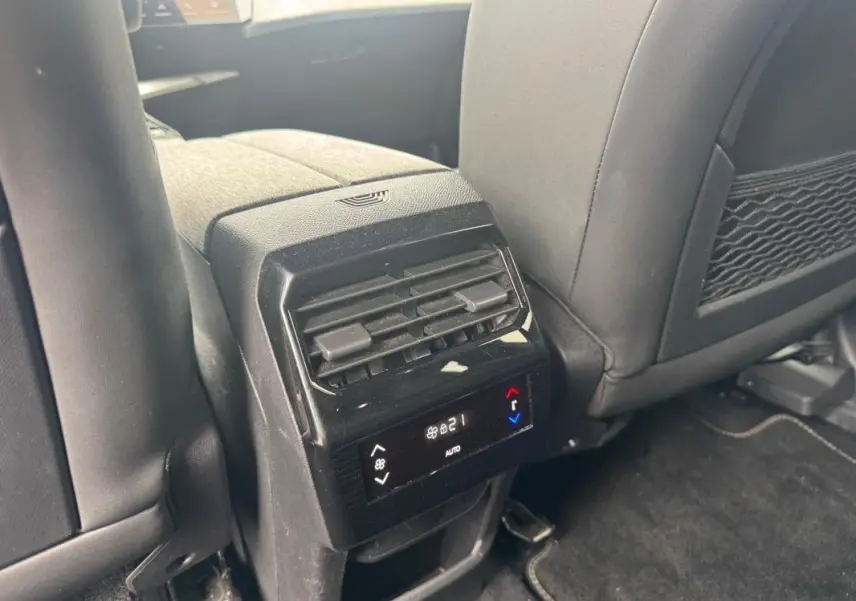 Vue rapprochée de la console arrière noire du Peugeot 5008 Hybrid 2025 avec commandes climatisation et sièges tissu.