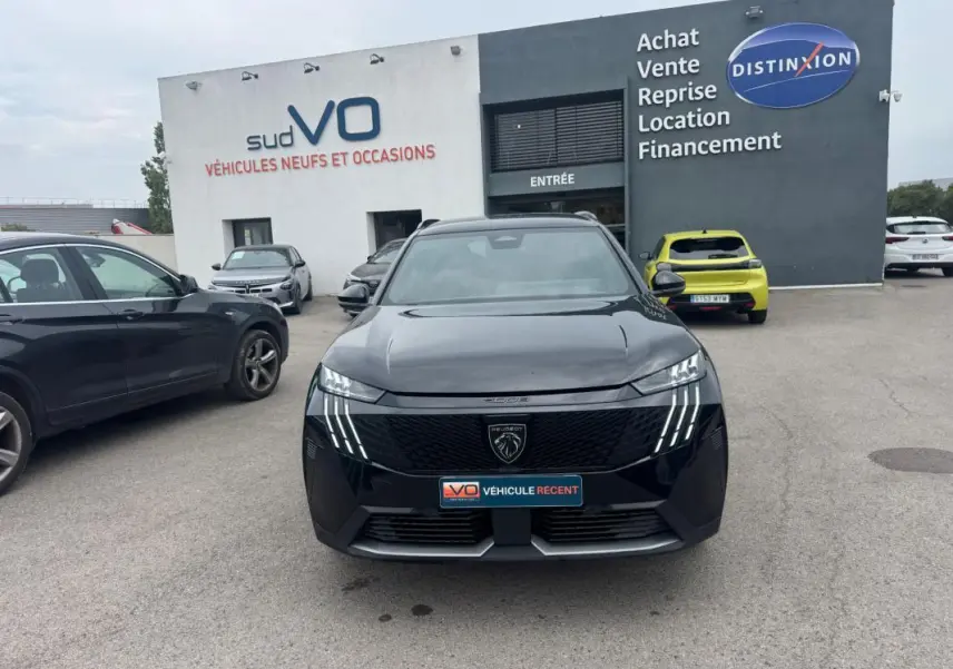 Vue avant d’un Peugeot 5008 Hybrid noir 2025 avec calandre distinctive et feux LED en griffes, stationné devant un concessionnaire.