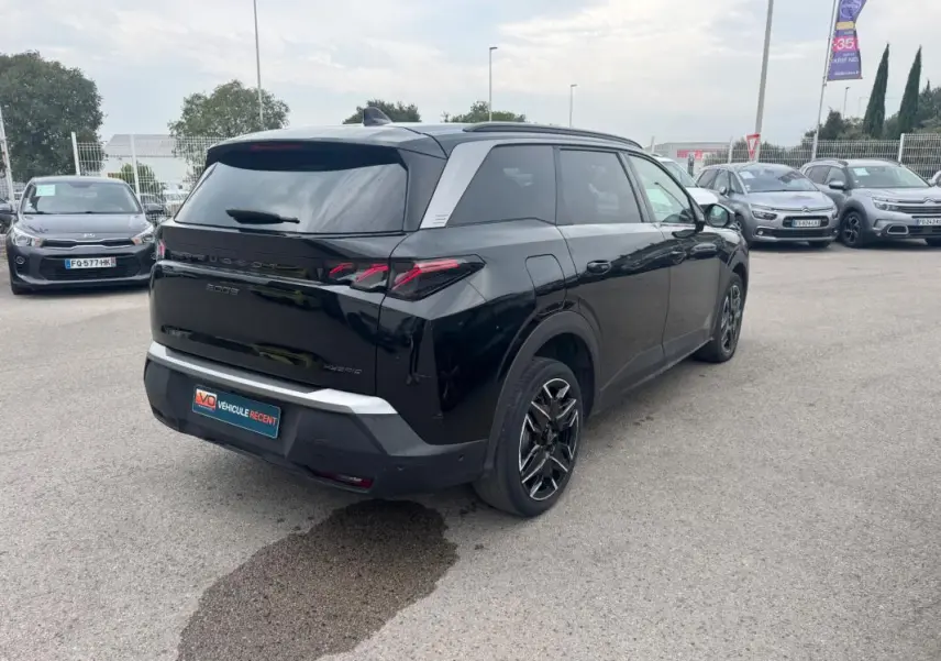 Vue 3/4 arrière droite d’un Peugeot 5008 Hybrid noir avec jantes alliage 19 pouces et barres de toit visibles.