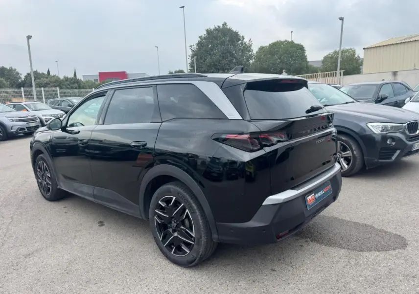 Vue 3/4 arrière droite d’un Peugeot 5008 noir avec jantes alliage noires et barres de toit visibles en extérieur.