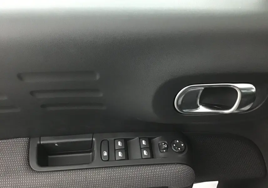 Gros plan sur la porte côté gauche de la Citroën C3 Aircross gris platinium, montrant les commandes des vitres et la poignée chrome.