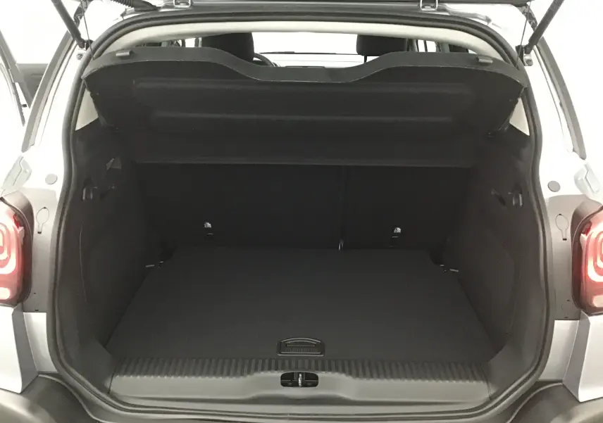 Coffre ouvert vu de l'arrière d'un Citroën C3 Aircross gris platinium avec intérieur noir et feux arrière allumés.