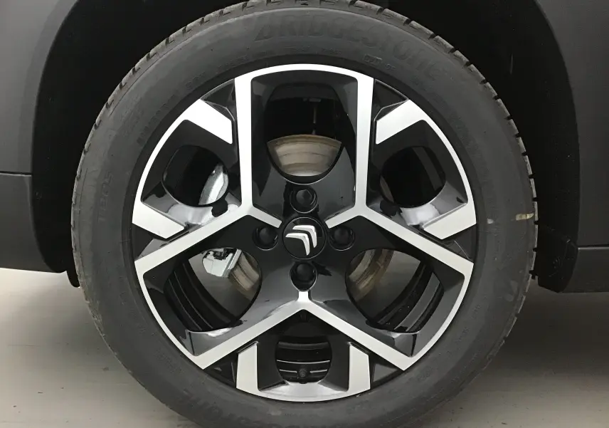Gros plan sur la jante alliage noire et argentée avec logo Citroën du côté gauche d’un C3 Aircross gris platinium.