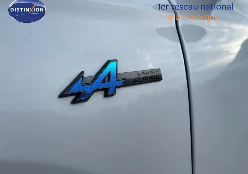 Gros plan sur l'écusson bleu Esprit Alpine sur la portière blanche nacrée d'un Renault Austral 2025 hybride.