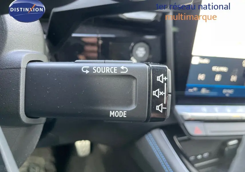 Gros plan sur la commande audio au volant du Renault Austral blanc nacré, avec tableau de bord et écran tactile en arrière-plan.