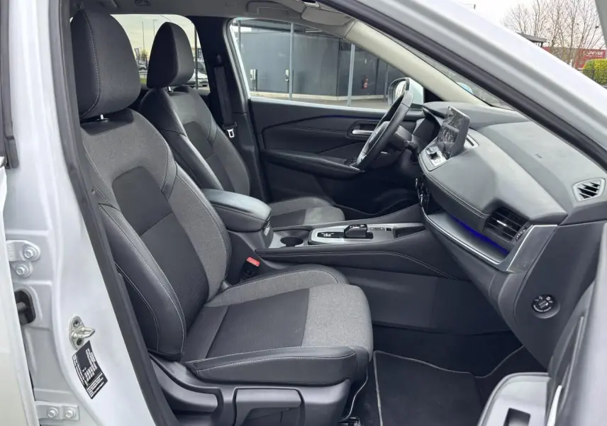Vue intérieure côté conducteur du Nissan Qashqai blanc nacré 2025, sièges tissu noir et gris avec console centrale moderne.