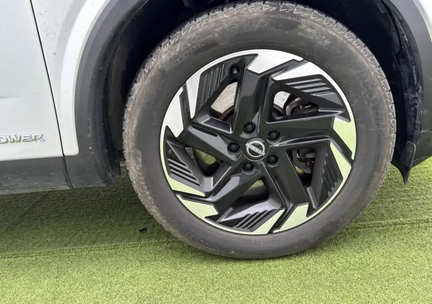 Gros plan sur la roue avant droite du Nissan Qashqai blanc nacré avec jante alliage noire et argentée.