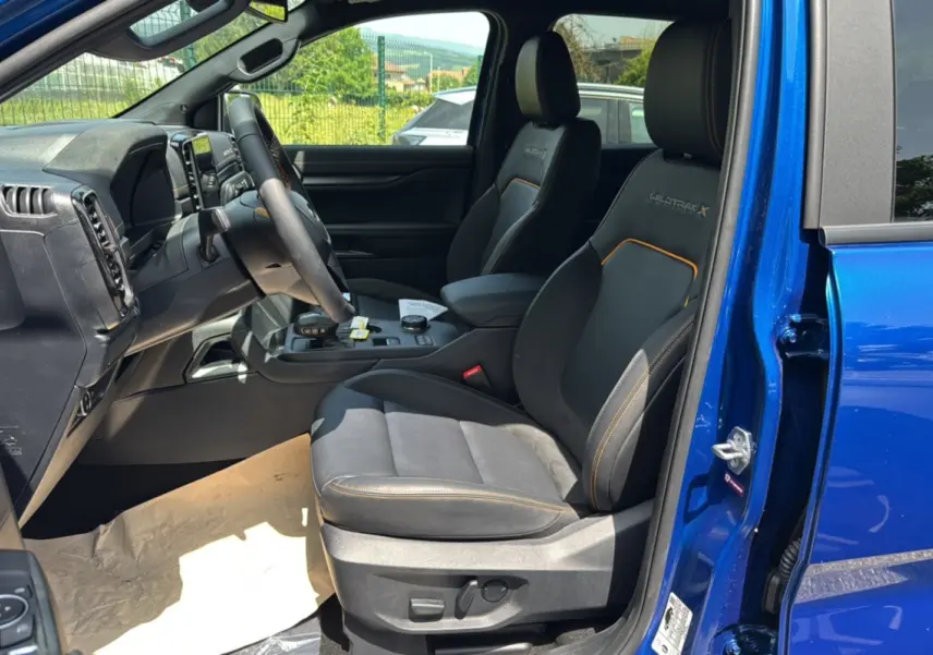 Vue intérieure côté conducteur du Ford Ranger 2025 bleu lightning, sièges Wildtrak X avec surpiqûres orange et volant cuir multifonctions.