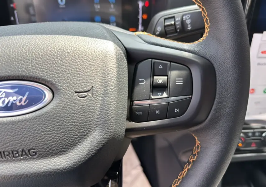 Gros plan sur le volant cuir noir avec surpiqûres orange du Ford Ranger 205 Wildtrak X, boutons multifonctions visibles.
