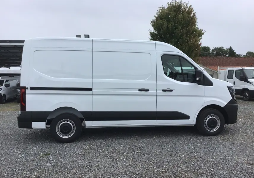 Vue de profil côté droit d’un Renault Master blanc L2H2 2025 avec bande noire et jantes acier sur un sol gravillonné.