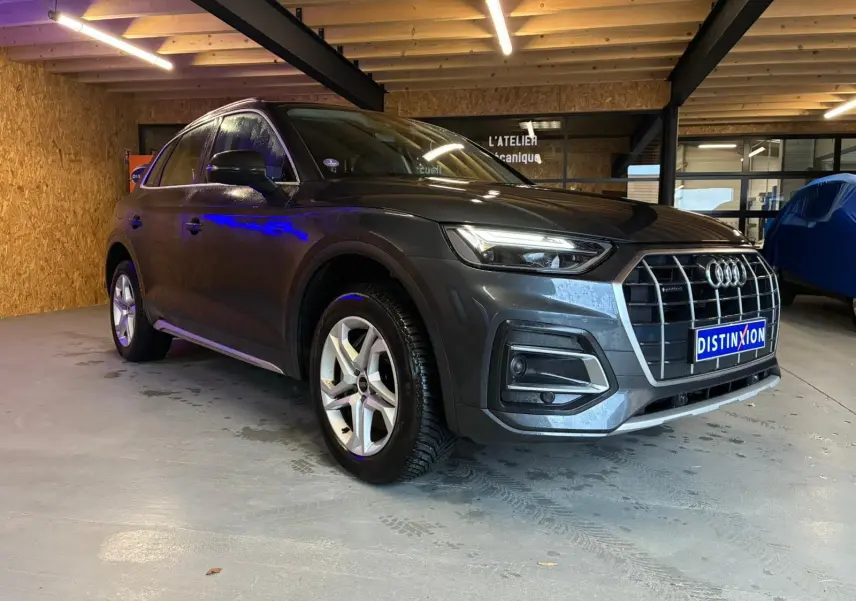 Audi Q5 gris hybride rechargeable vu en 3/4 avant droit dans un garage avec jantes 5 branches doubles.