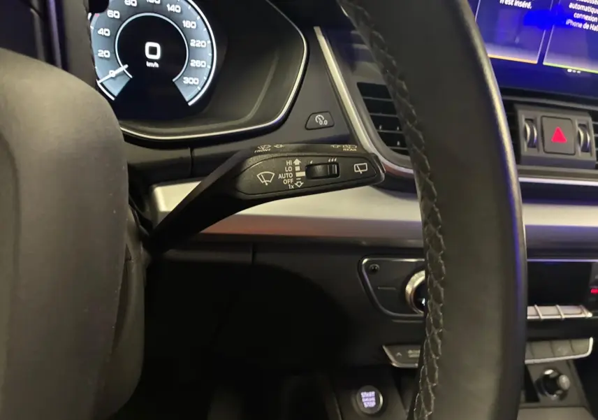 Gros plan sur le commodo de lève-glace à gauche du volant cuir d’un Audi Q5 gris hybride rechargeable 2024.