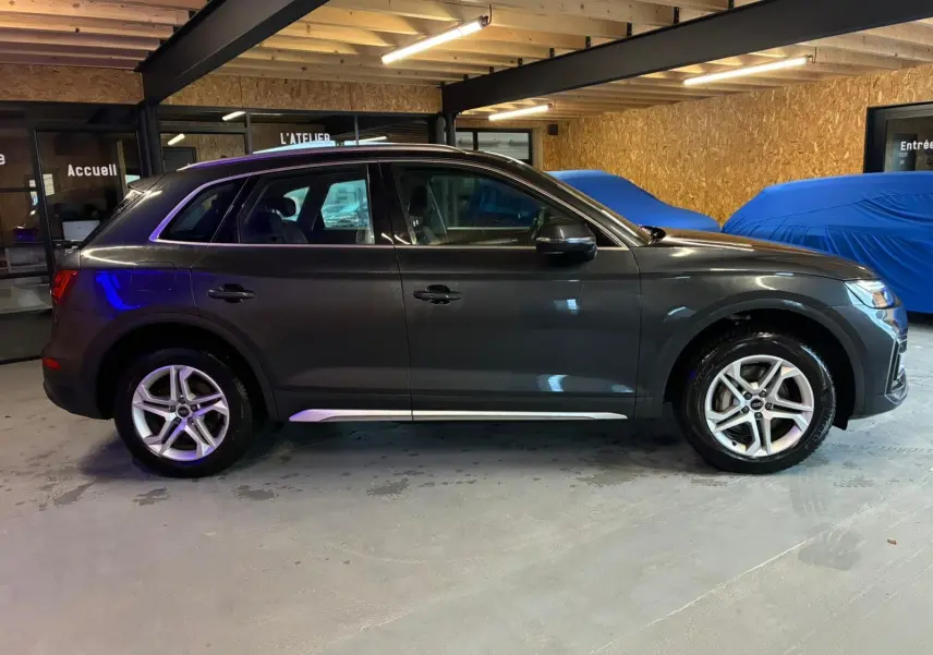 Audi Q5 gris vue de profil côté gauche dans un garage, avec jantes 5 branches doubles et moulures argentées.