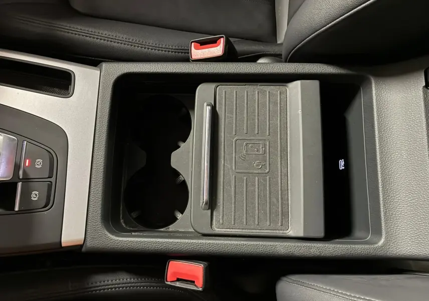 Vue plongeante sur la console centrale noire de l'Audi Q5 2024 avec porte-gobelets et chargeur sans fil.