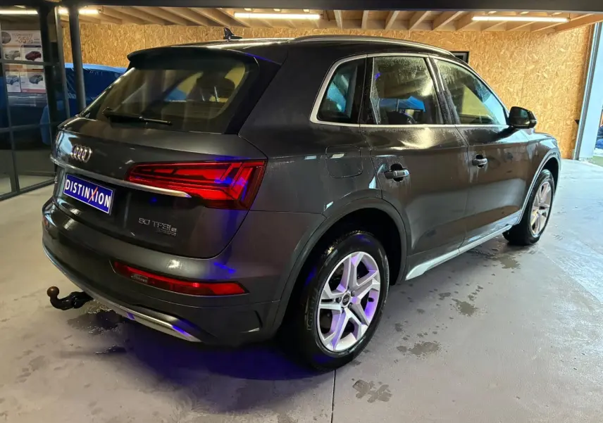 Audi Q5 gris en vue 3/4 arrière droit, avec jantes 5 branches doubles et crochet d'attelage visible.