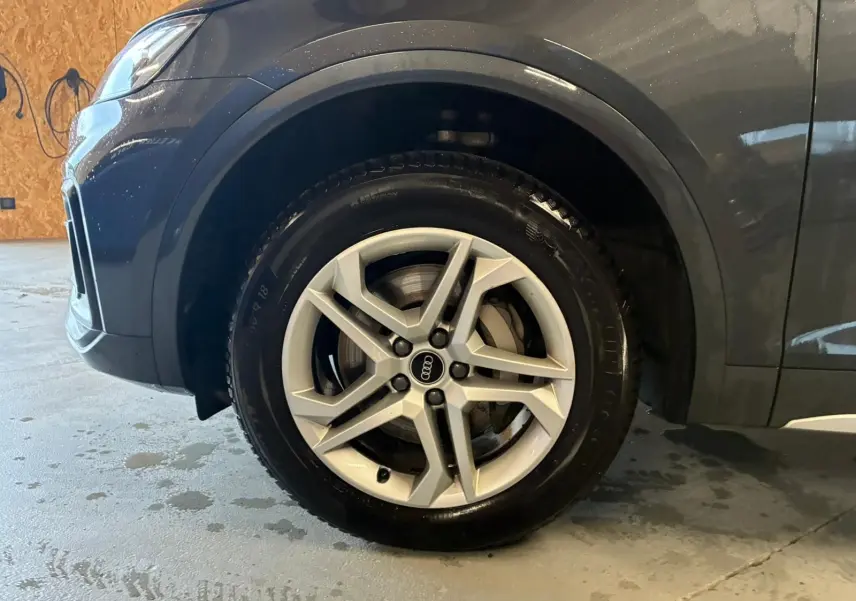 Vue de côté droit avant sur l’Audi Q5 gris avec passage de roue noir grainé et partie avant visible en intérieur.