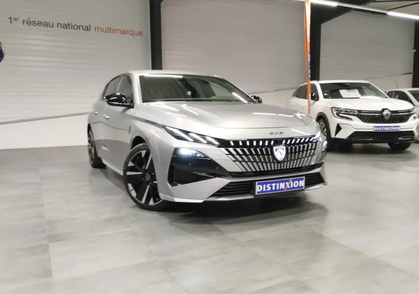 Vue 3/4 avant d'une Peugeot 308 gris Artense avec calandre lumineuse et jantes alliage noires en showroom.