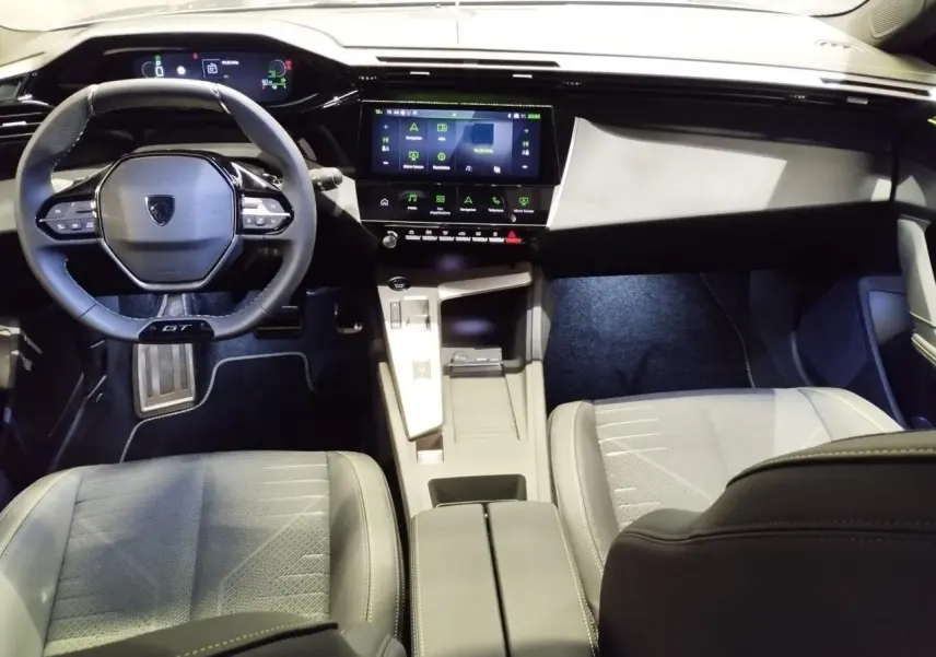 Vue intérieure avant de la Peugeot 308 GT 2026, tableau de bord noir avec écran tactile et volant compact GT cuir.